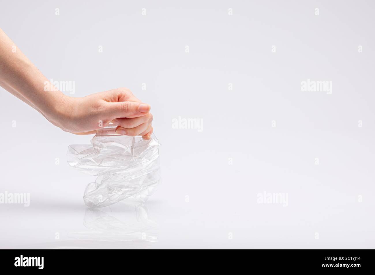 Nahaufnahme einer weißen Menschenhand, die vor einem weißen Hintergrund eine zerknitterte Plastikflasche zermalmt Stockfoto