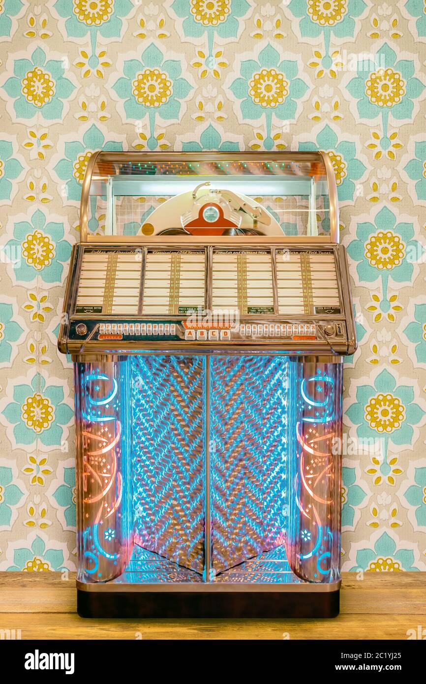 Bunte Vintage Jukebox vor Retro-Blumen-Tapete auf einem Holzboden Stockfoto