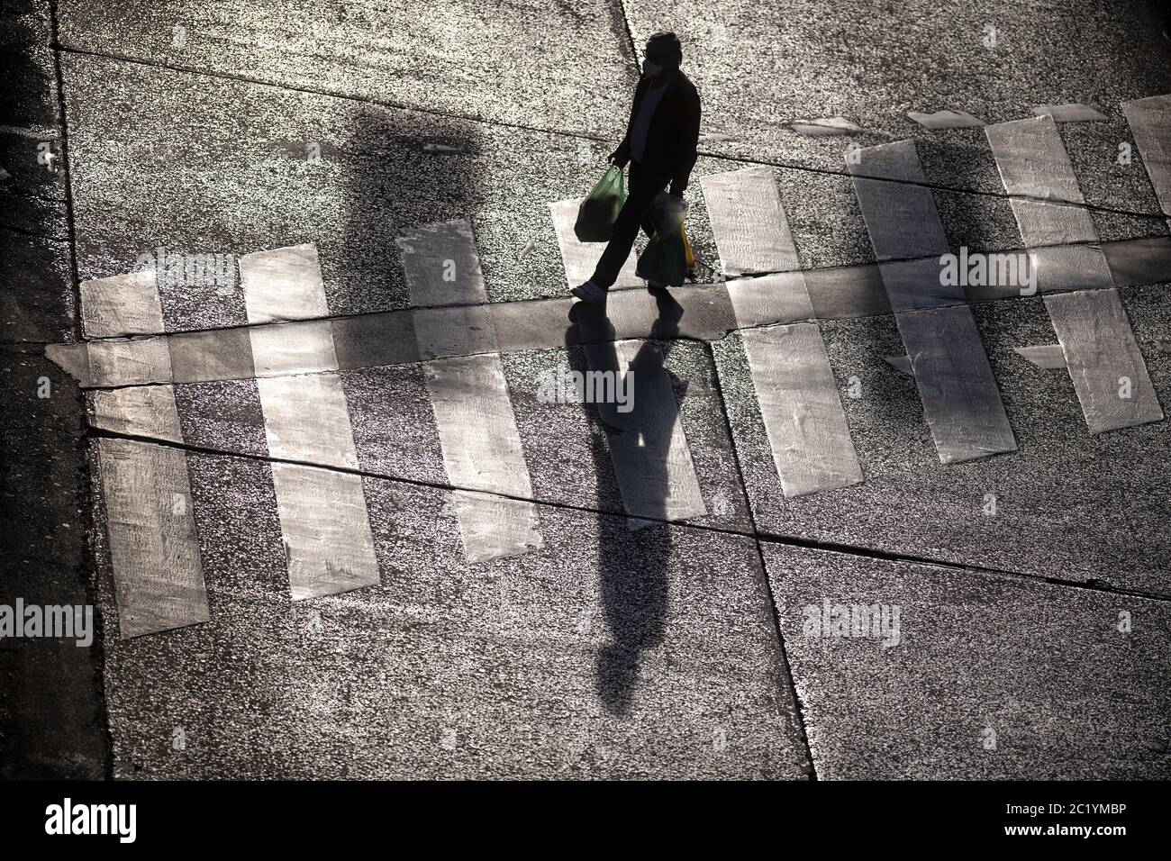 Draufsicht auf einen Silhouettenmenschen und seine Schattenüberquerung Der Fußgängerüberweg Stockfoto