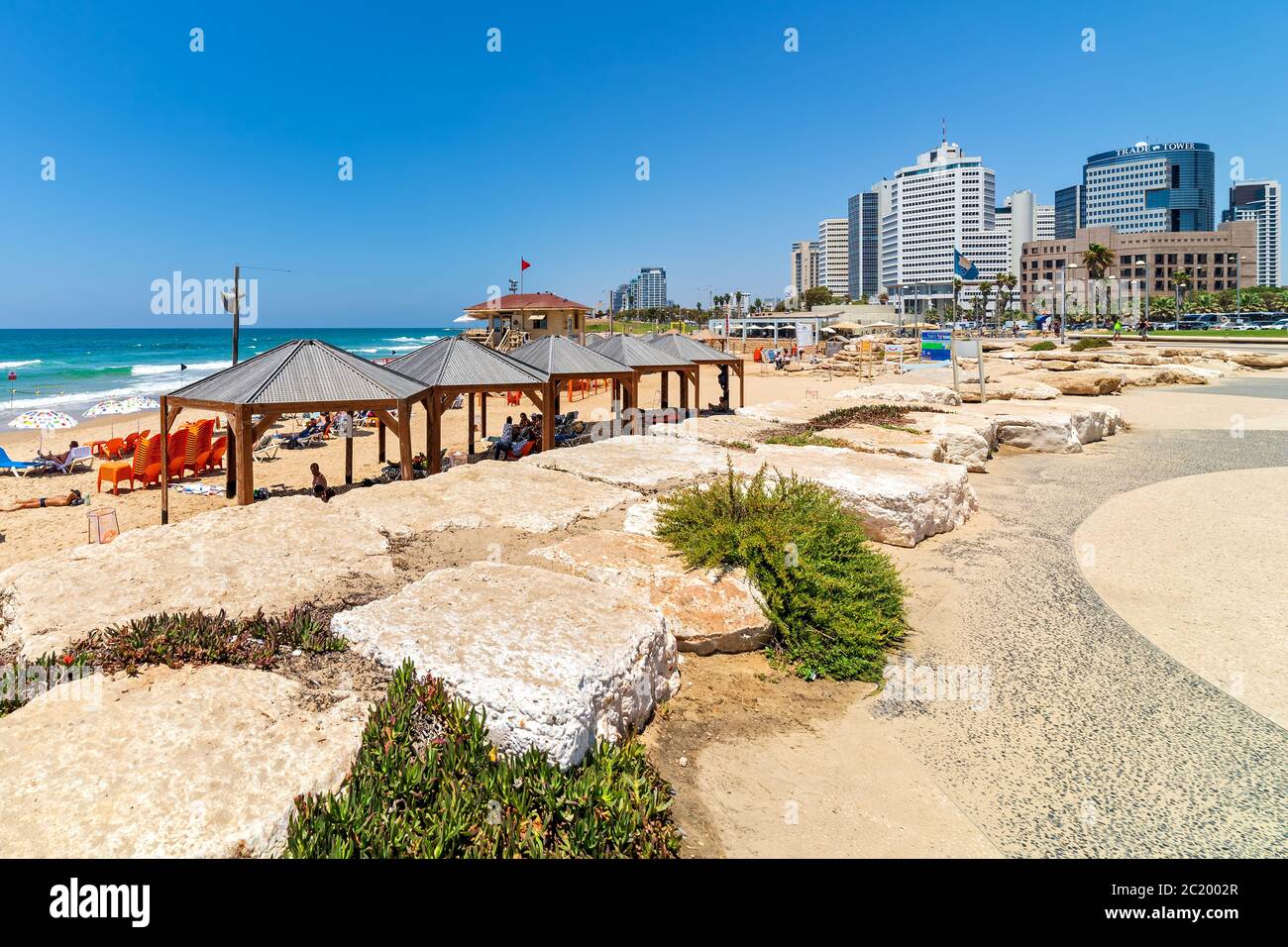 Blick auf die Promenade am öffentlichen Strand als moderne Geschäftsgebäude im Hintergrund unter blauem Himmel in Tel Aviv, Israel. Stockfoto