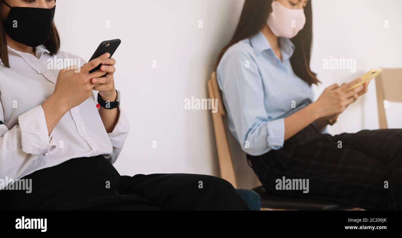 Zwei asiatische junge Frau chatten im Smartphone und tragen Maske sitzende Entfernung schützen vor COVID-19-Viren für soziale Distanzierung für Infektionsrisiko. Stockfoto