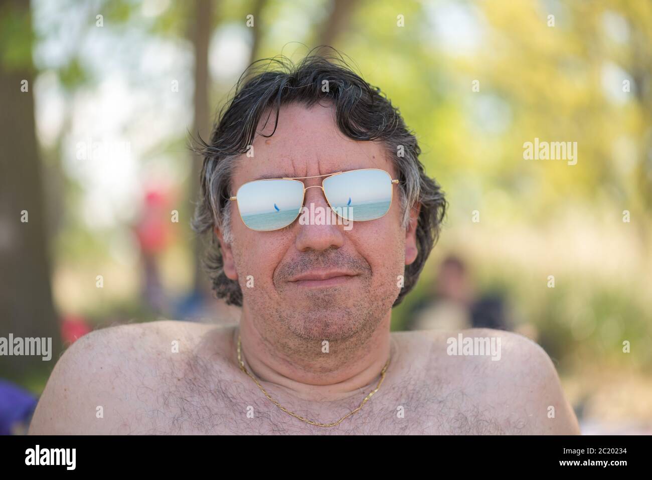 Porträt eines Mannes mit Sonnenbrille und Spiegelung eines Bootes in einem See Stockfoto