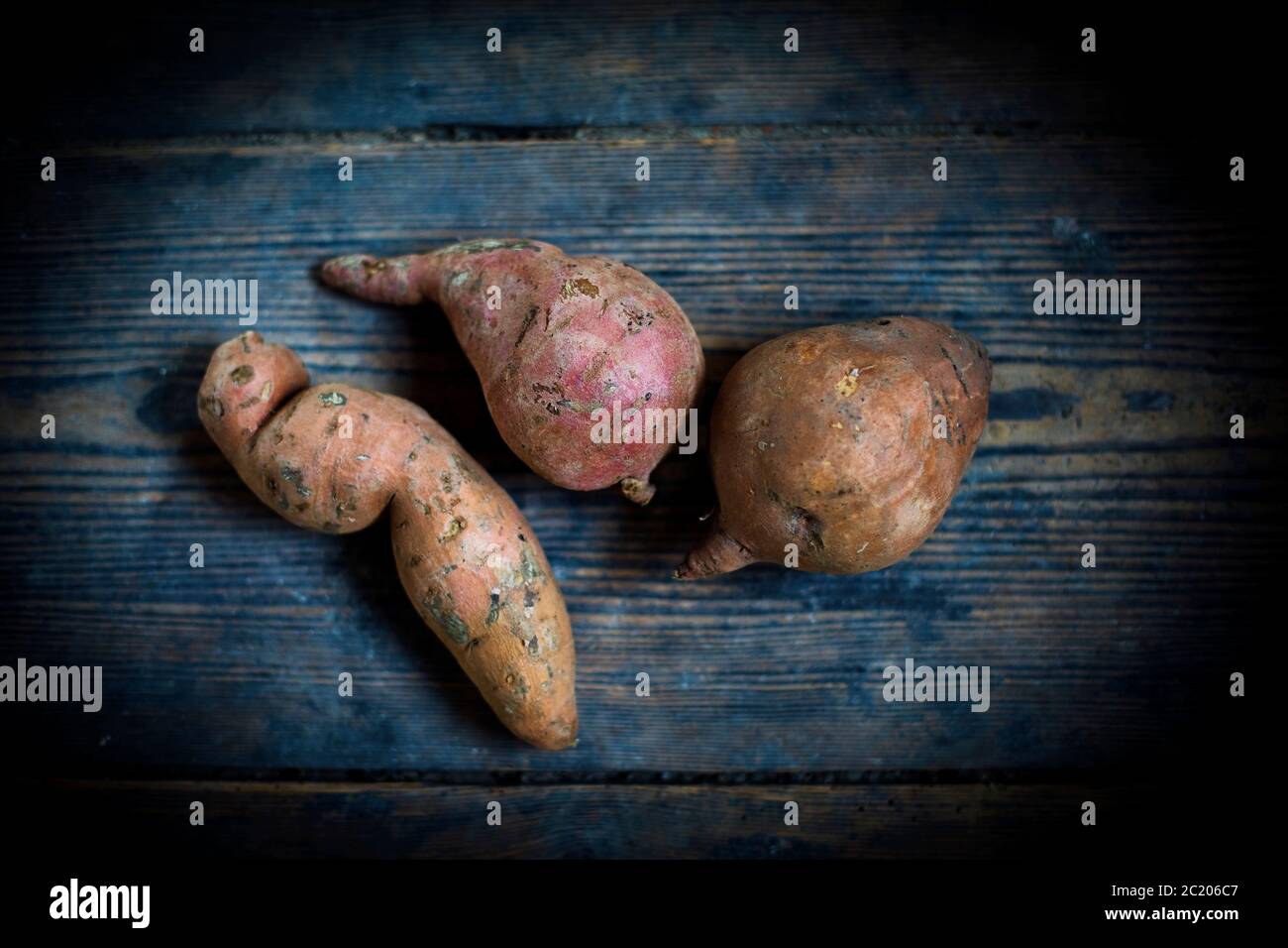 Rohe Süßkartoffeln auf einem dunkelblauen Holzbrett Stockfoto
