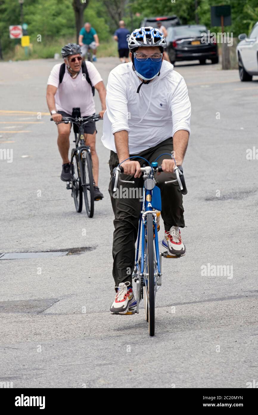 Radfahrer fahren auf einem Pfad in der Nähe des Cross Island Parkway in Bayside, Queens, NYC. Einer trägt eine Maske, die anderen nicht. Stockfoto