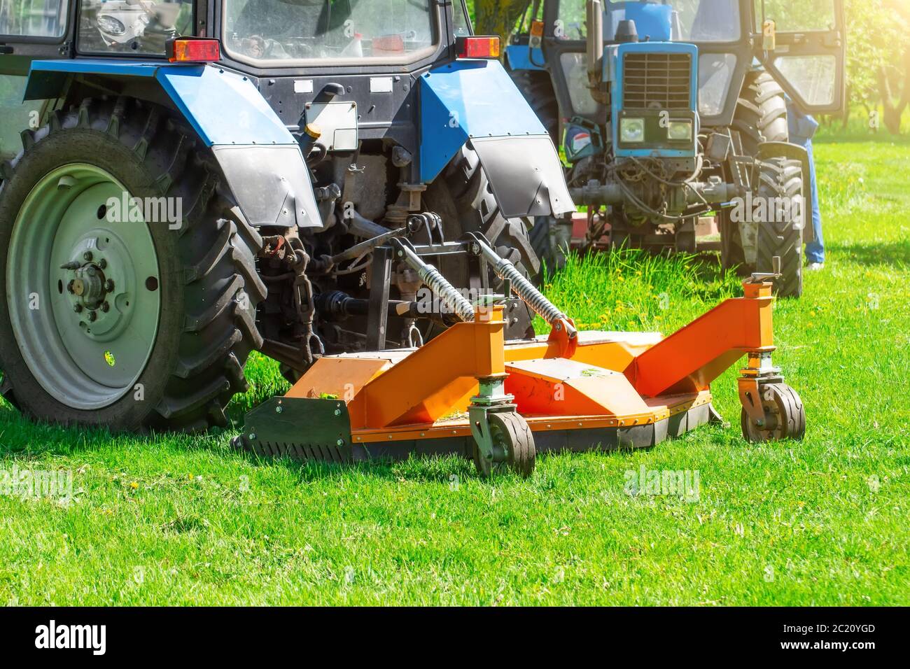 Traktor verwendet gezogene Rasenmäher, um Gras auf Stadtrasen zu mähen, Rückansicht Stockfoto