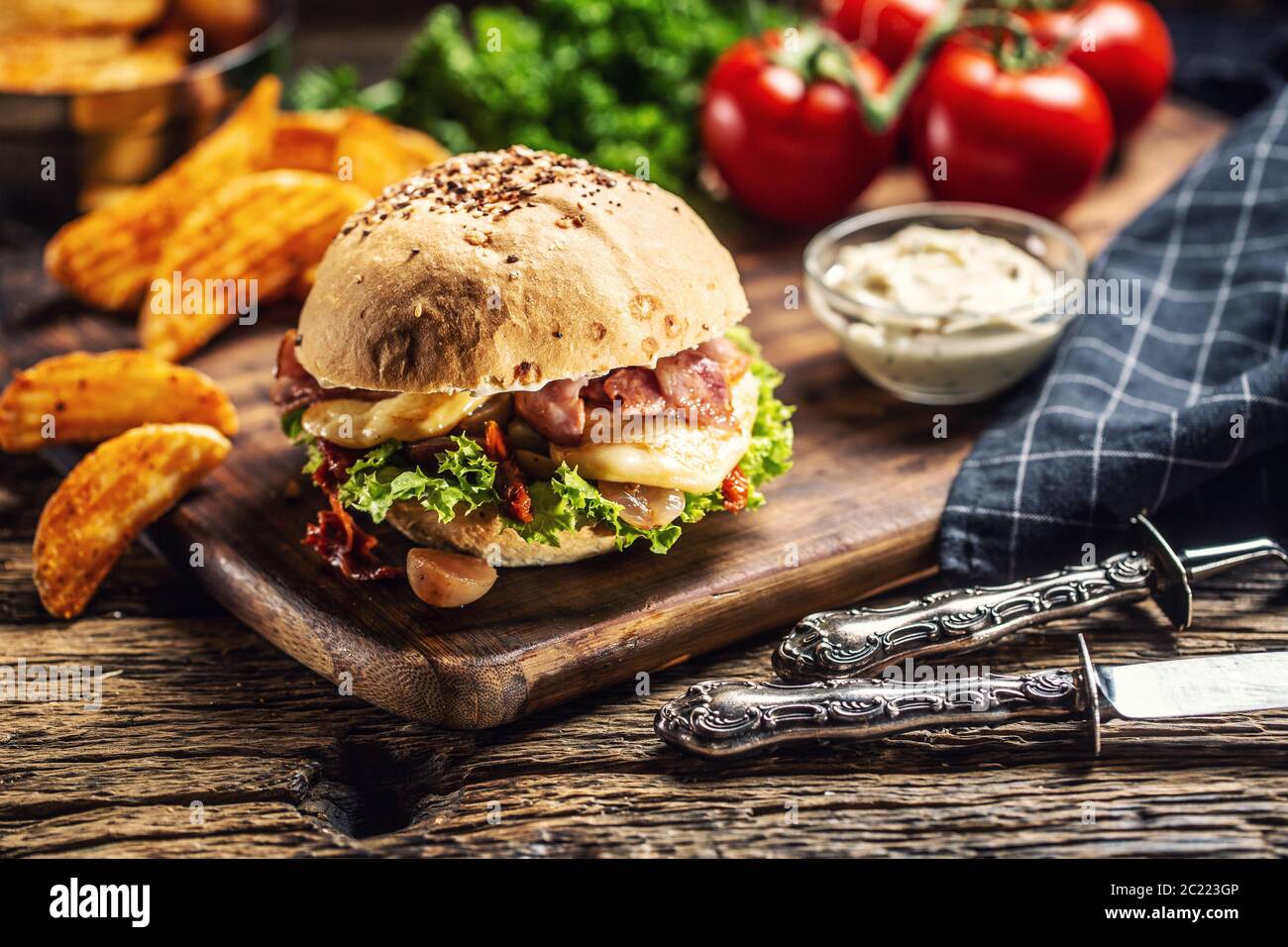 Doppelter Käseburger mit Speck und Salat in einem Sesambrötchen mit Kartoffelkeilen und Mayo auf der Seite Stockfoto