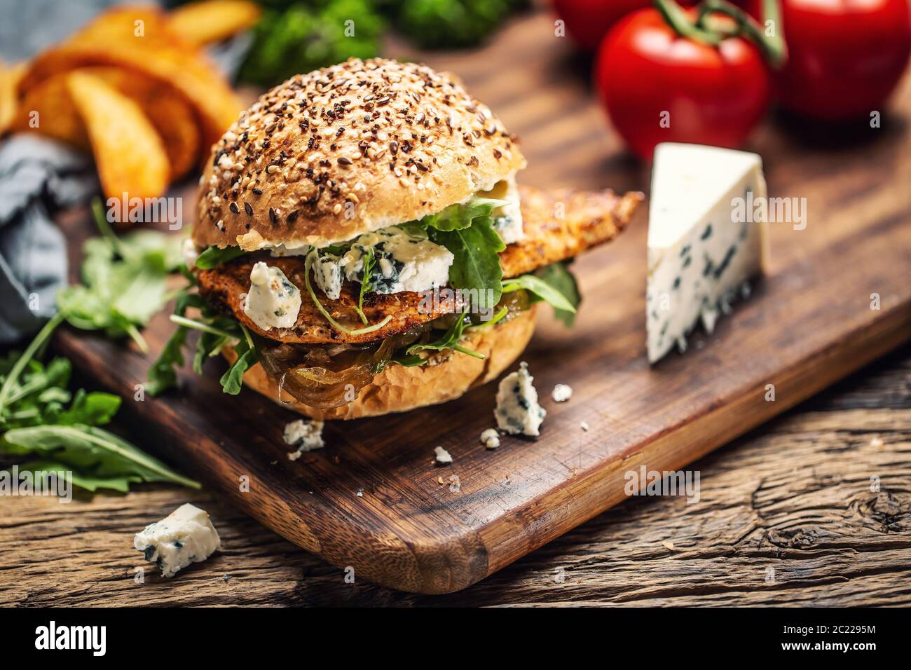 Hühnerburger mit Blauschimmelkäse und Rucola in einem Sesambrötchen auf einem rustikalen Holz Stockfoto