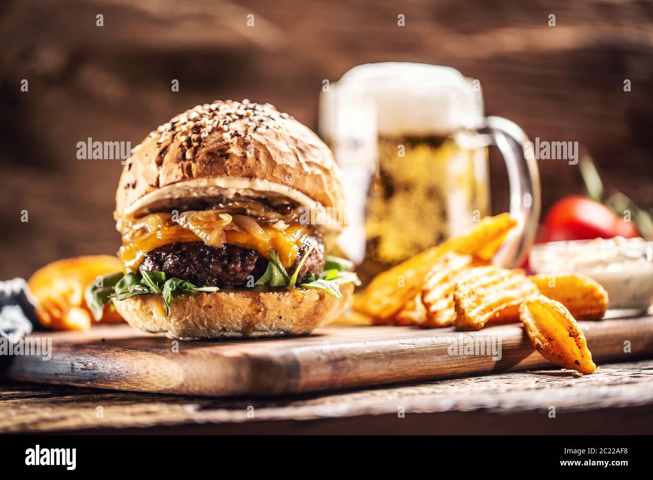 Rinderburger mit karamellisierten Zwiebeln, Rucola und geschmolzenem Käse mit Kartoffelkeilen und Fassbier im Hintergrund Stockfoto