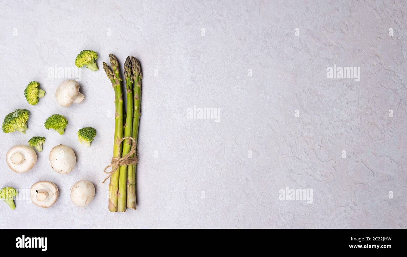 Gruppe von Bio-Gemüse - grüner Spargel, Brokkoli, Pilze auf grauem Hintergrund, flach legen. Konzept der gesunden vegetarischen Ernährung, Ernährung und h Stockfoto