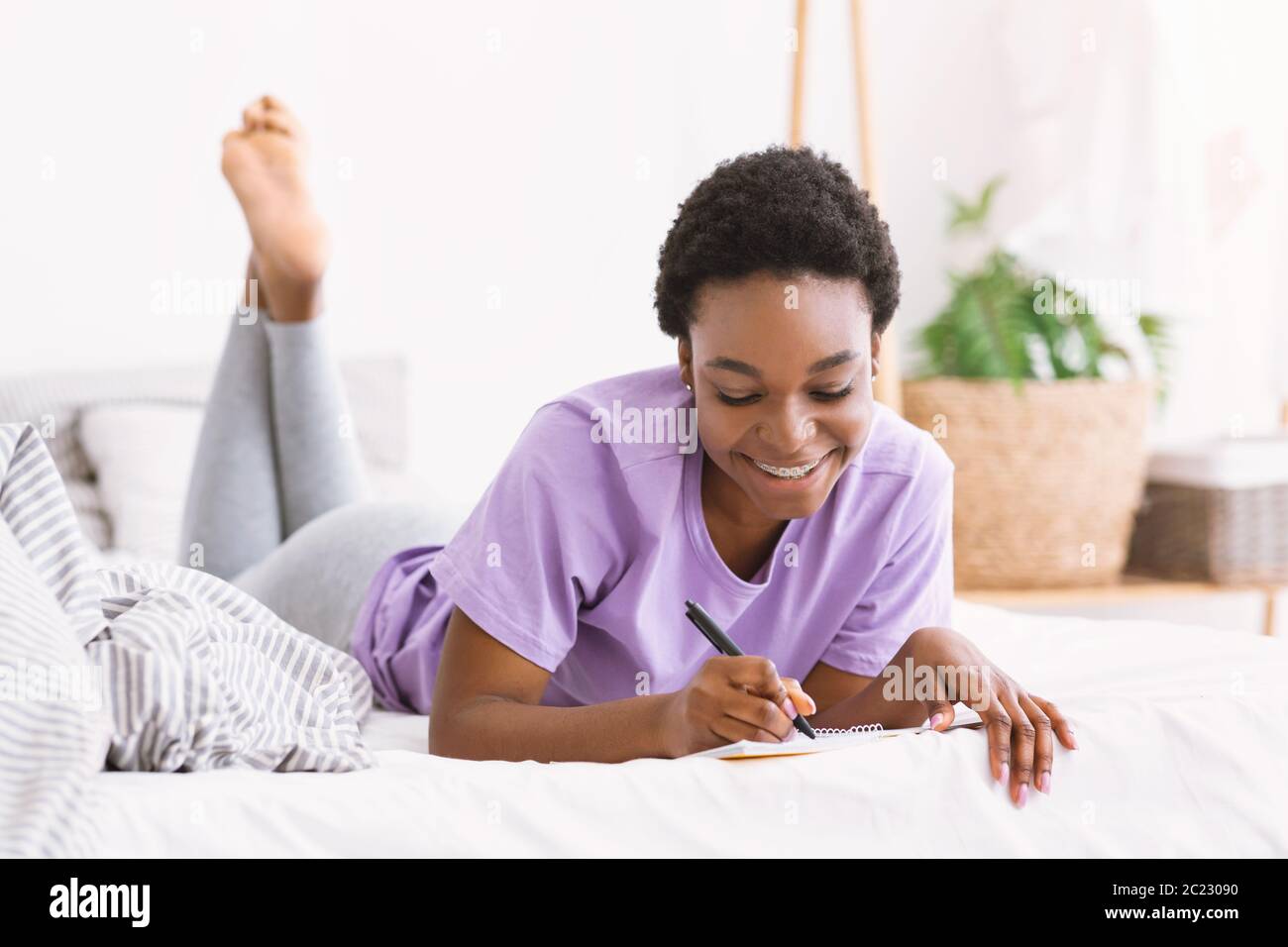 Führen Sie ein persönliches Tagebuch. Mädchen liegt auf dem Bett und schreibt im Notizbuch Stockfoto