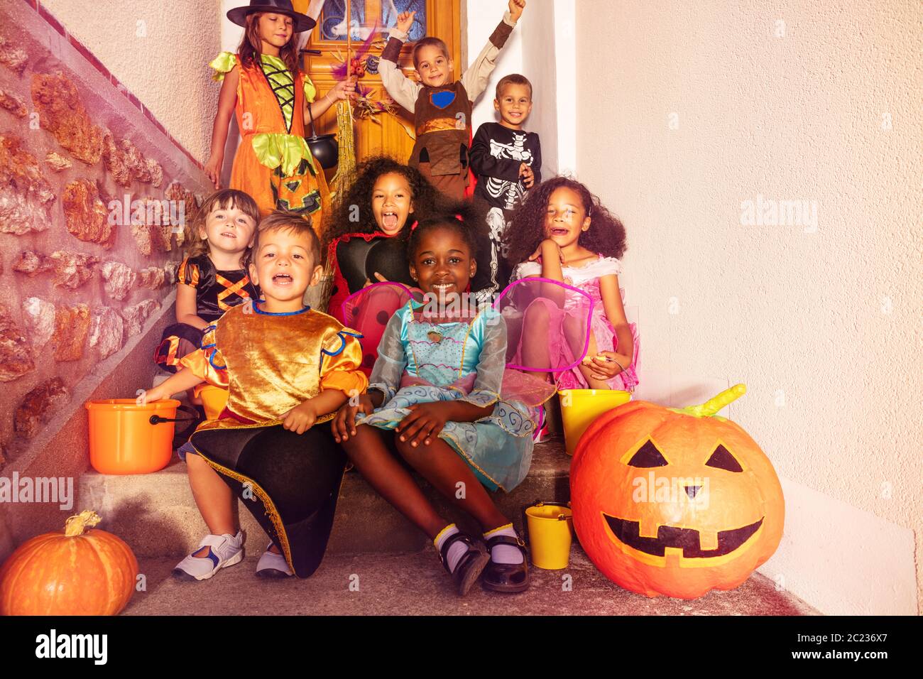 Große Gruppe von Halloween-Kinder in Kostümen sitzen auf der Treppe mit orangefarbenen Kürbis und Eimer lächeln Blick auf die Kamera Stockfoto