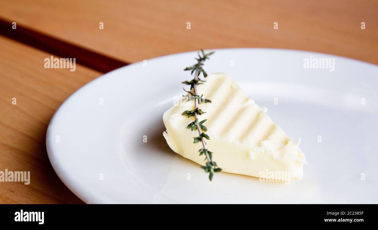 Individuelle Butter Dreieck mit Zweig Thymian Akzent auf kleinen weißen Teller zu Brot oder geeignete Vorspeise gelegt Stockfotografie