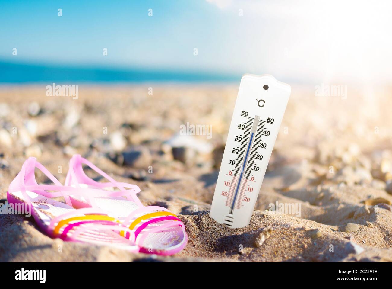 Sommerwetter und Hörkonzept, Thermometer im Sand am Strand gegen Meer und blauen Himmel Stockfoto