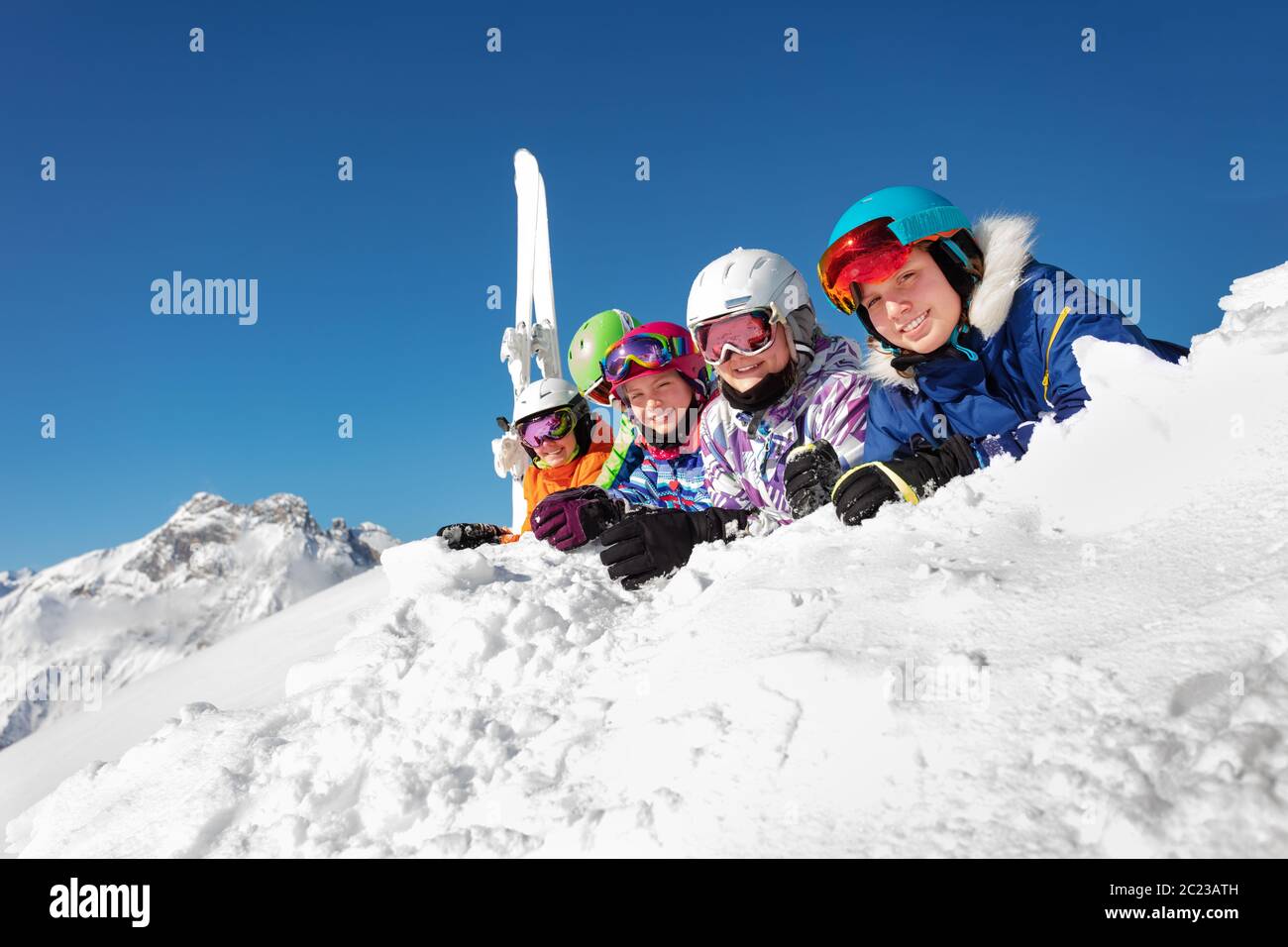 Große Gruppe von Ski-Kids lag auf Schnee fröhlich lächelnd über Berggipfel und blauen Himmel in bunten Sport-Outfit Stockfoto