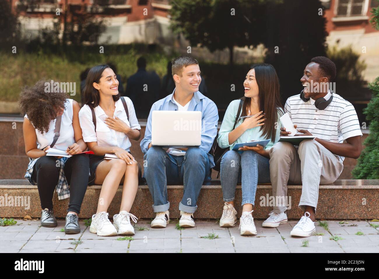 Pause Zwischen Den Klassen. Glückliche Studenten sitzen auf der Bank auf dem Universitätscampus Stockfoto
