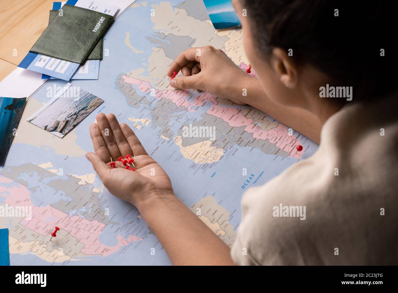 Über der Schulter sehen Sie Frau mit roten Pins, während Sie auf der Weltkarte Reisestorte markieren Stockfoto