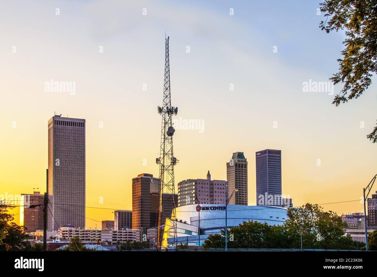 06-14-2020 Tulsa USA BOK Zentrum gegen Downtown Skyline bei Sonnenaufgang mit gelbem Himmel mit Kommunikationsturm Stockfoto