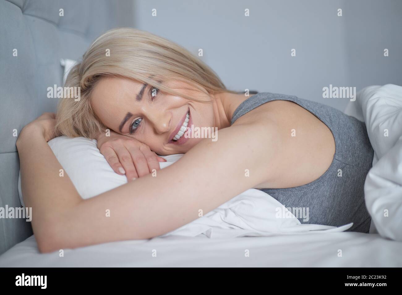 Lächelnd lässig blond liegt in ihrem Bett in hellen Schlafzimmer Stockfoto
