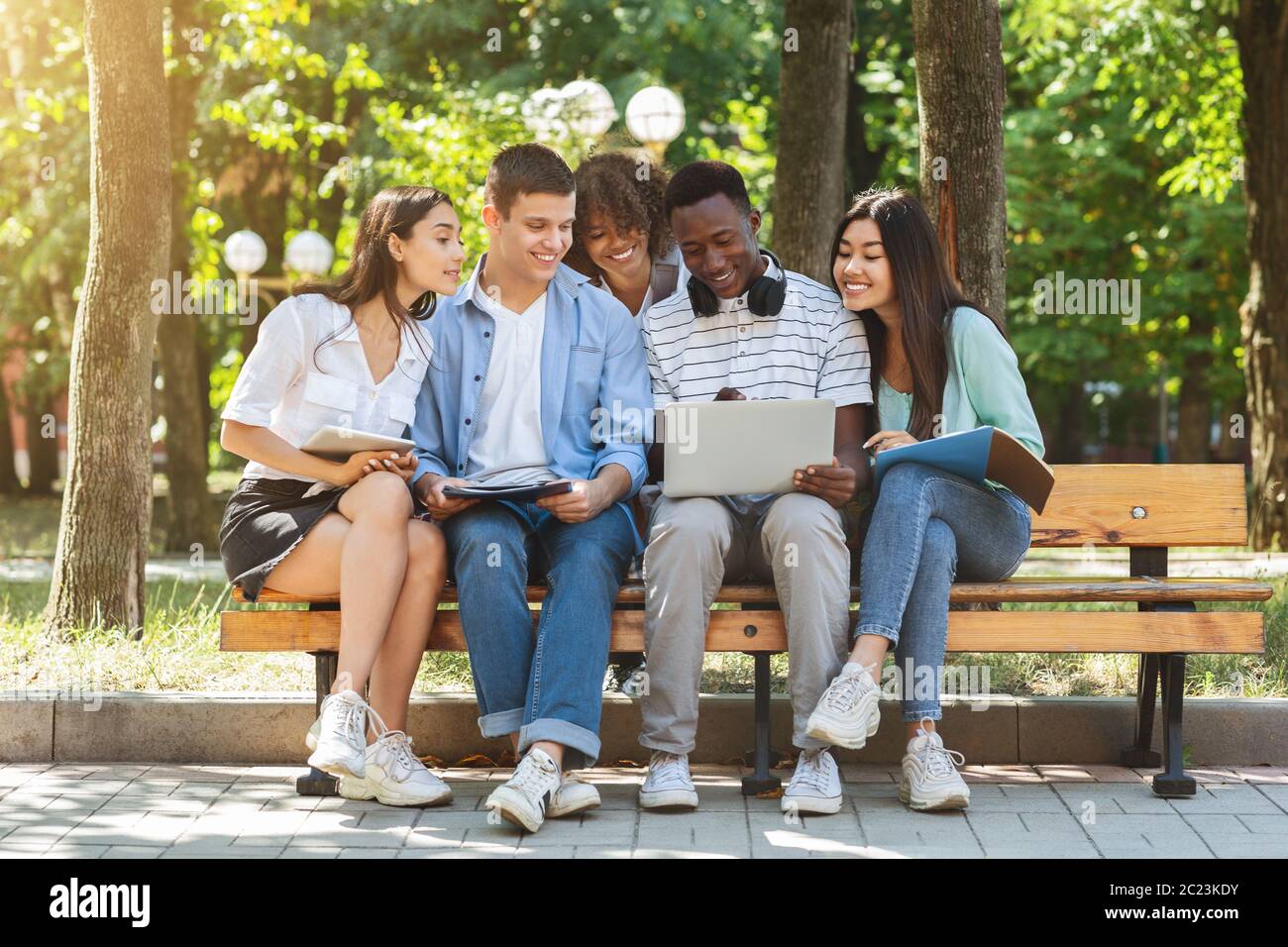 Multiethnische College-Freunde, die sich im Freien auf dem Campus ausruhen und zusammen einen Laptop verwenden Stockfoto