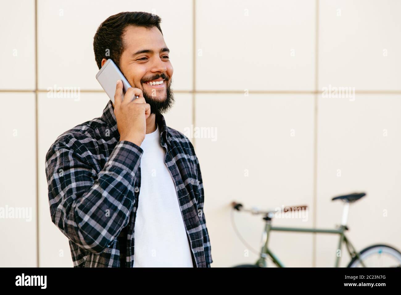 Freundliche stilvolle junger bärtiger Mann per Handy kommunizieren, angenehmes Gespräch, beim Stehen im Freien in der Nähe des Rad. Stockfoto
