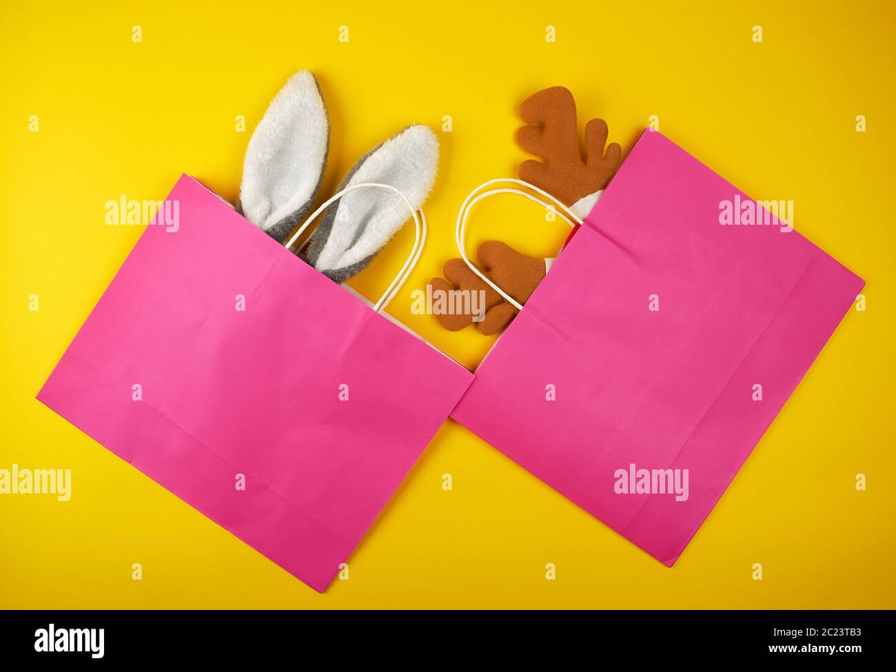 Zwei rosa Papier taschen zum Einkaufen, innerhalb der Weihnachten Maske von einem Kaninchen und einem Reh auf gelbem Hintergrund, flach Stockfoto