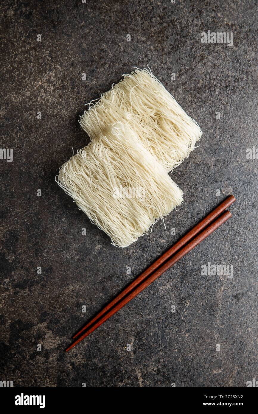 Ungekochte weiße Reisnudeln und Essstäbchen auf schwarzem Tisch. Draufsicht. Stockfoto