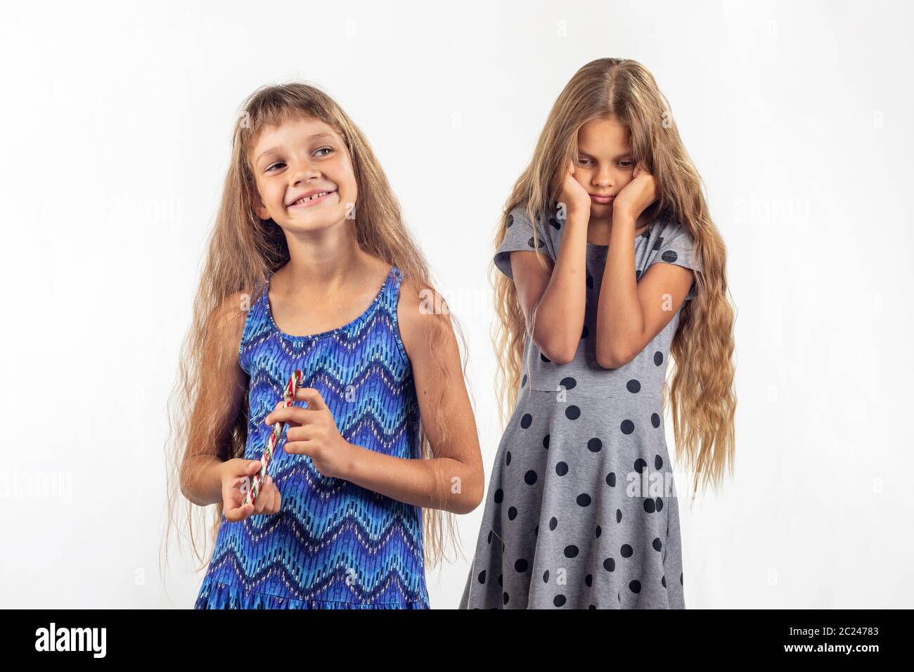 Mädchen hält freudig Süßigkeit, traurig, andere Mädchen im Hintergrund Stockfoto