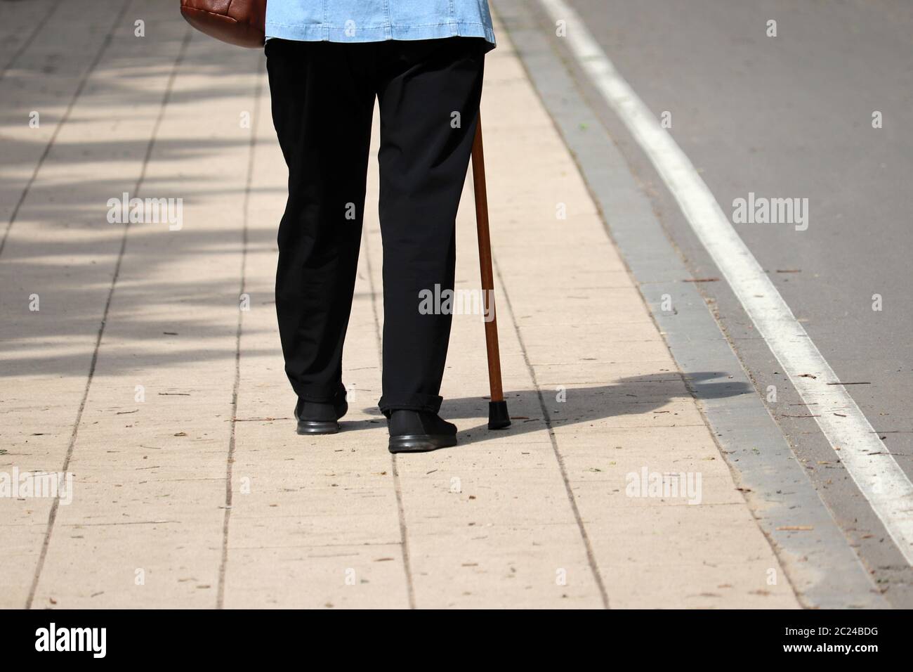 Frau, die mit einem Stock auf einer Straße geht, weibliche Beine auf dem Bürgersteig. Konzept für Behinderung, hinkende Person, Erkrankungen der Wirbelsäule, alte Menschen Stockfoto