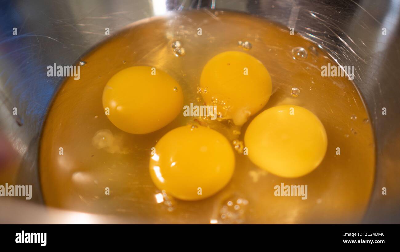Gelbe Eier auf Metallschüssel. Vier Eigelb für Hühnereier. Vorbereitung für Rühreier in einer Metallschüssel. Eier kochen Stockfoto