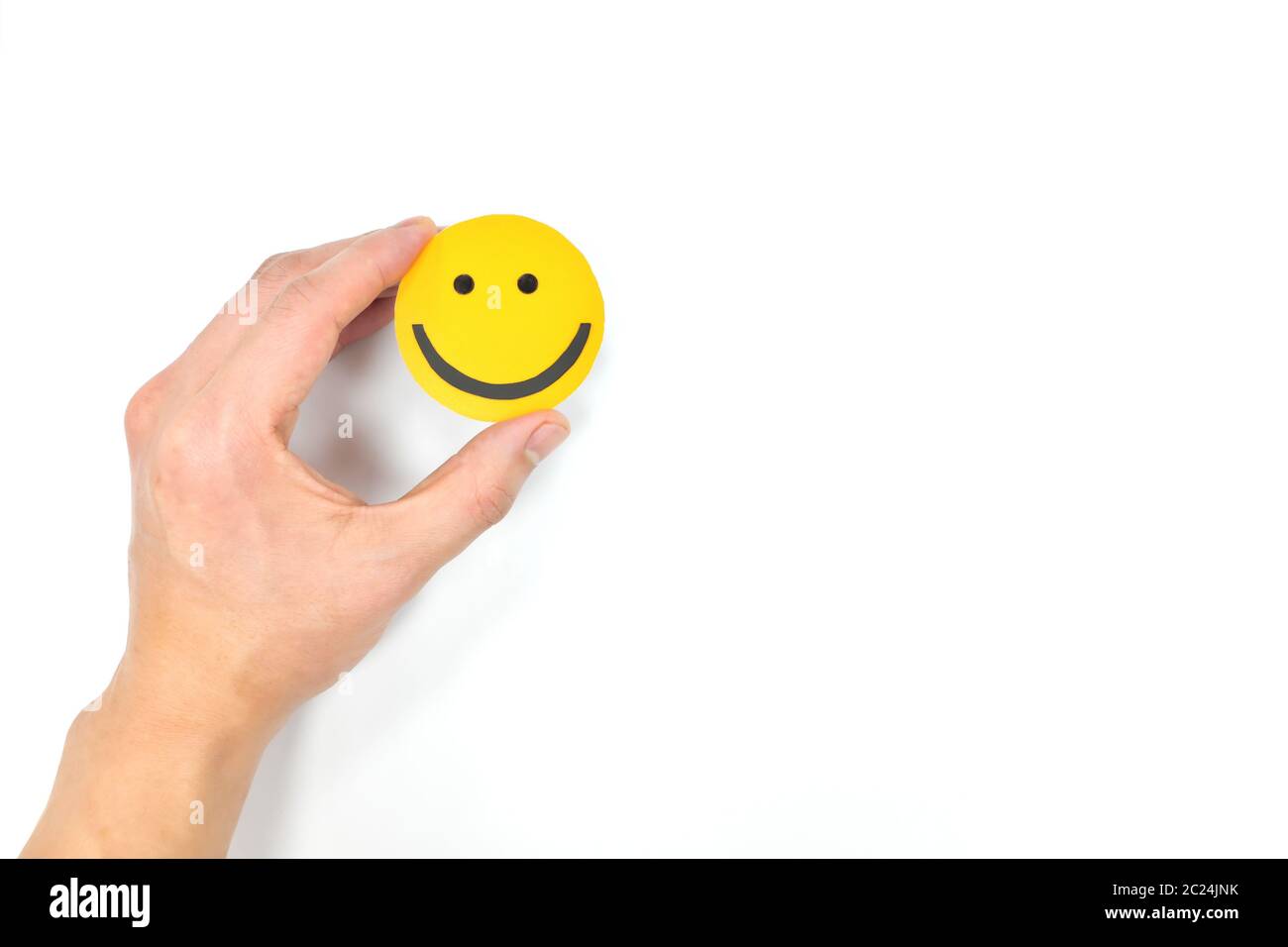 Glück und Positivität Konzept. Hand hält gelb lächelndes Gesicht in weißem Hintergrund mit Kopierraum. Stockfoto