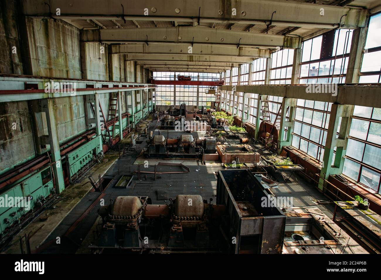 Alte verlassene überwucherte Fabrik mit verrostenen Resten von Industriemaschinen in der Werkstatt. Stockfoto