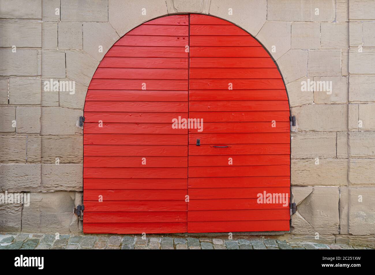 Rotes, frisch bemaltes rundes Holztor in einer alten Steinfassade Stockfoto