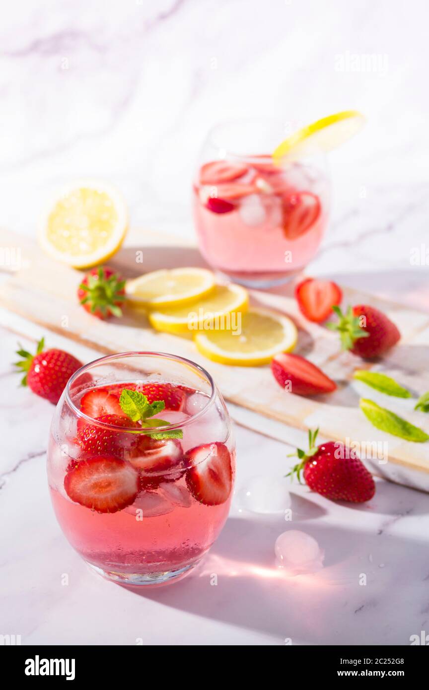 Gin und Tonic mit kaltrosa Erdbeer-Geschmack, garniert mit frischen Früchten, Zitronen- und Minzblättern. Stockfoto