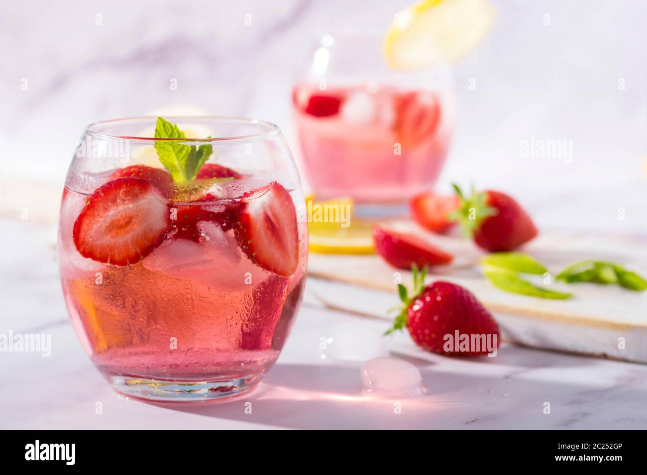 Gin und Tonic mit kaltrosa Erdbeer-Geschmack, garniert mit frischen Früchten, Zitronen- und Minzblättern. Stockfoto