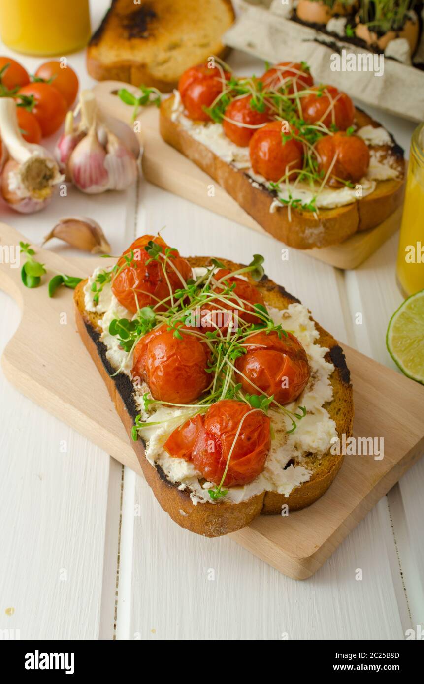 Geröstete Kirschtomatensoße und Ricotta auf Toast, frisch gepresster Orangensaft mit Limette, Bio-Knoblauch und Mikrogemüse auf Tomaten, gebacken mit Thymian Stockfoto