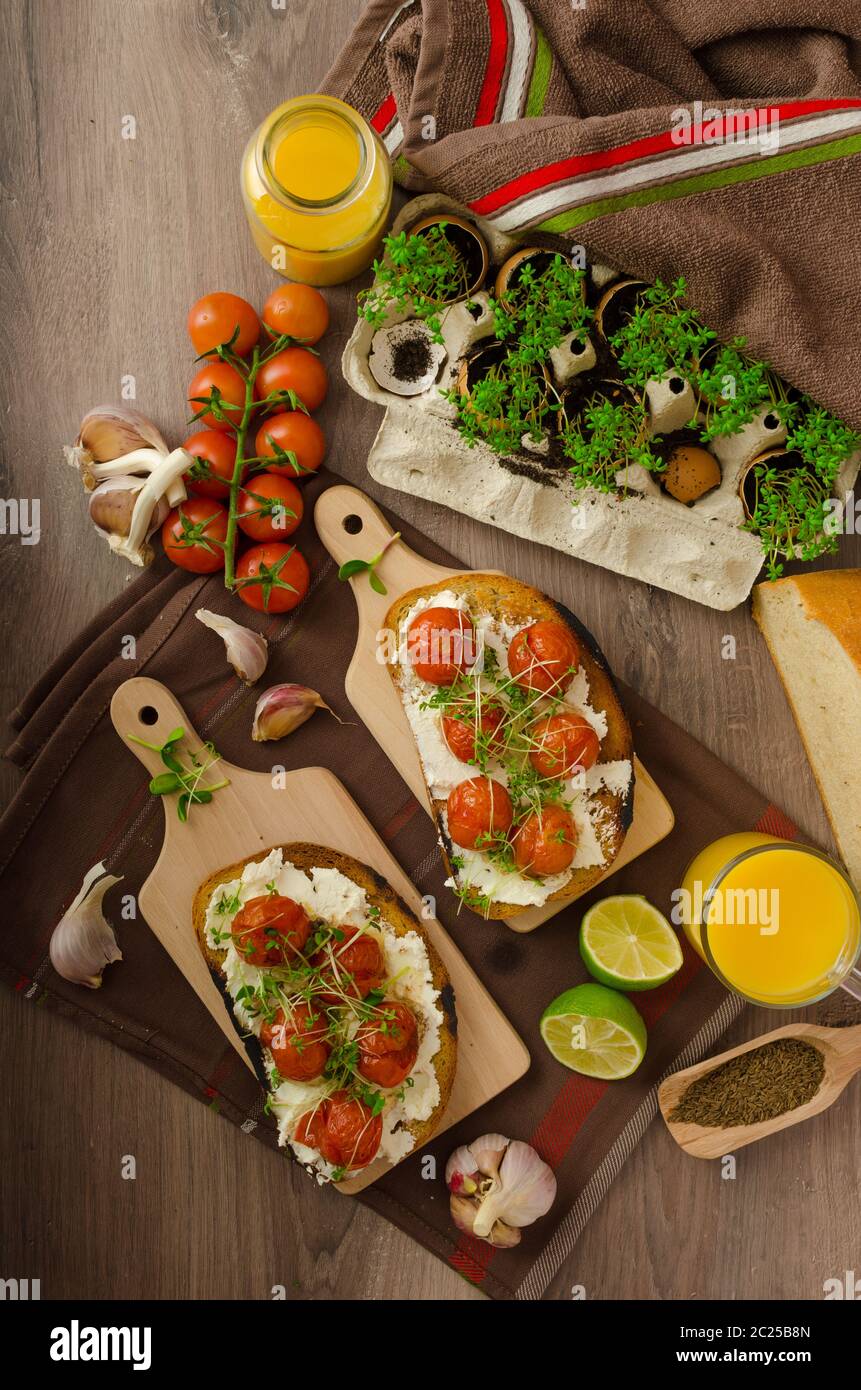 Geröstete Kirschtomatensoße und Ricotta auf Toast, frisch gepresster Orangensaft mit Limette, Bio-Knoblauch und Mikrogemüse auf Tomaten, gebacken mit Thymian Stockfoto