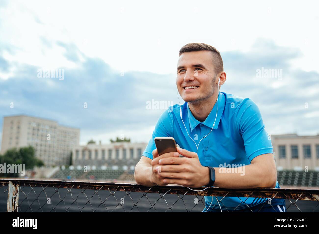 Lächelnd glückliche junge Menschen Musik hören, während sein Handy Holding, starrte in die Ferne, in lässig gekleidet, im Freien Stockfoto
