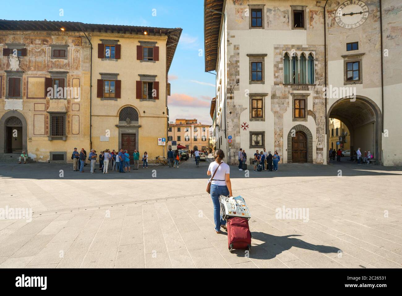 Eine weibliche Touristen, die alleine unterwegs ist und einen Gepäckkoffer auf Rädern im historischen Zentrum von Pisa, Italien, zieht. Stockfoto
