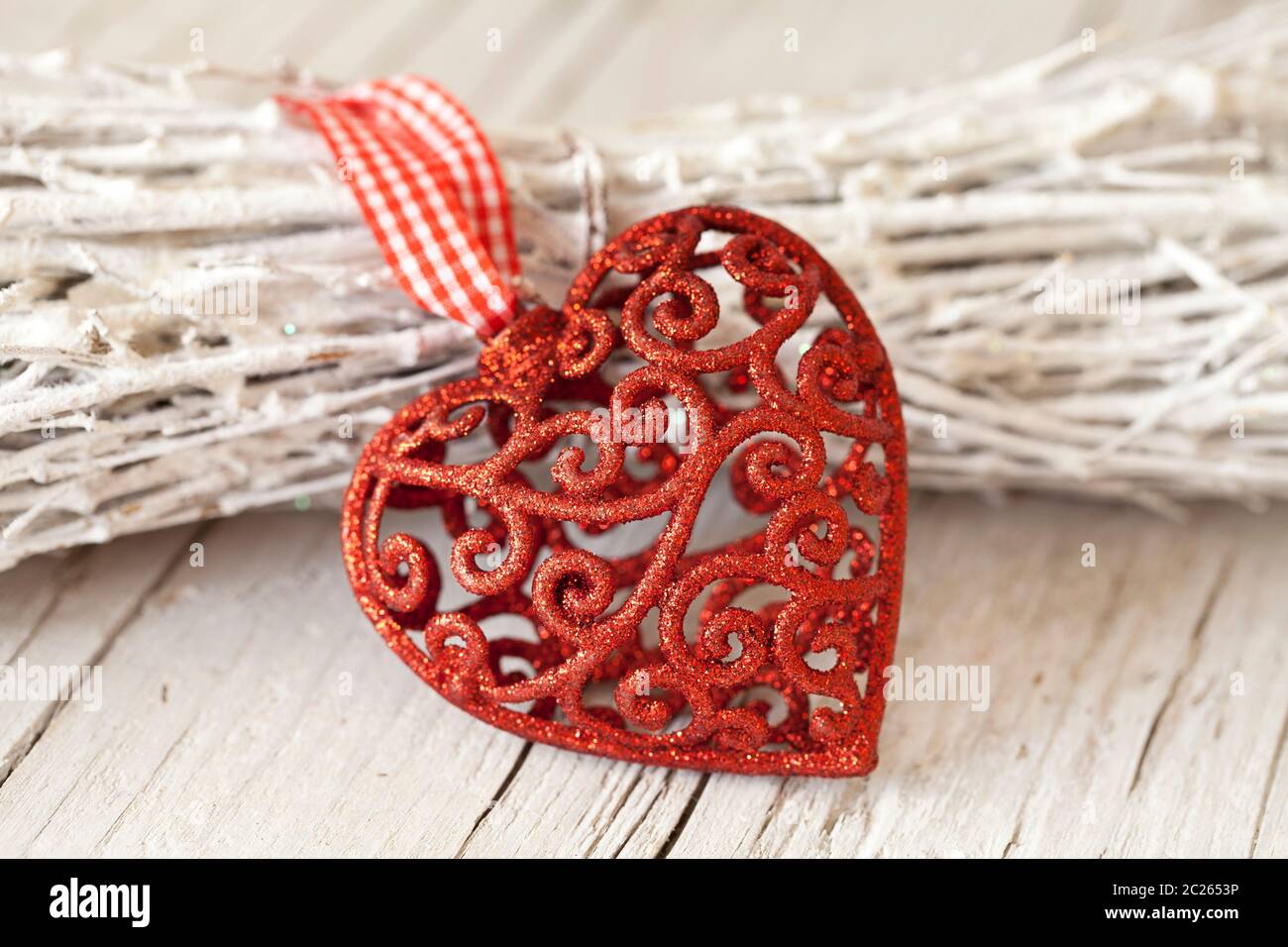 nordisches Weihnachtsstillleben mit rotem Ornament Herz, das sich auf Weidenbündel stützt Stockfoto
