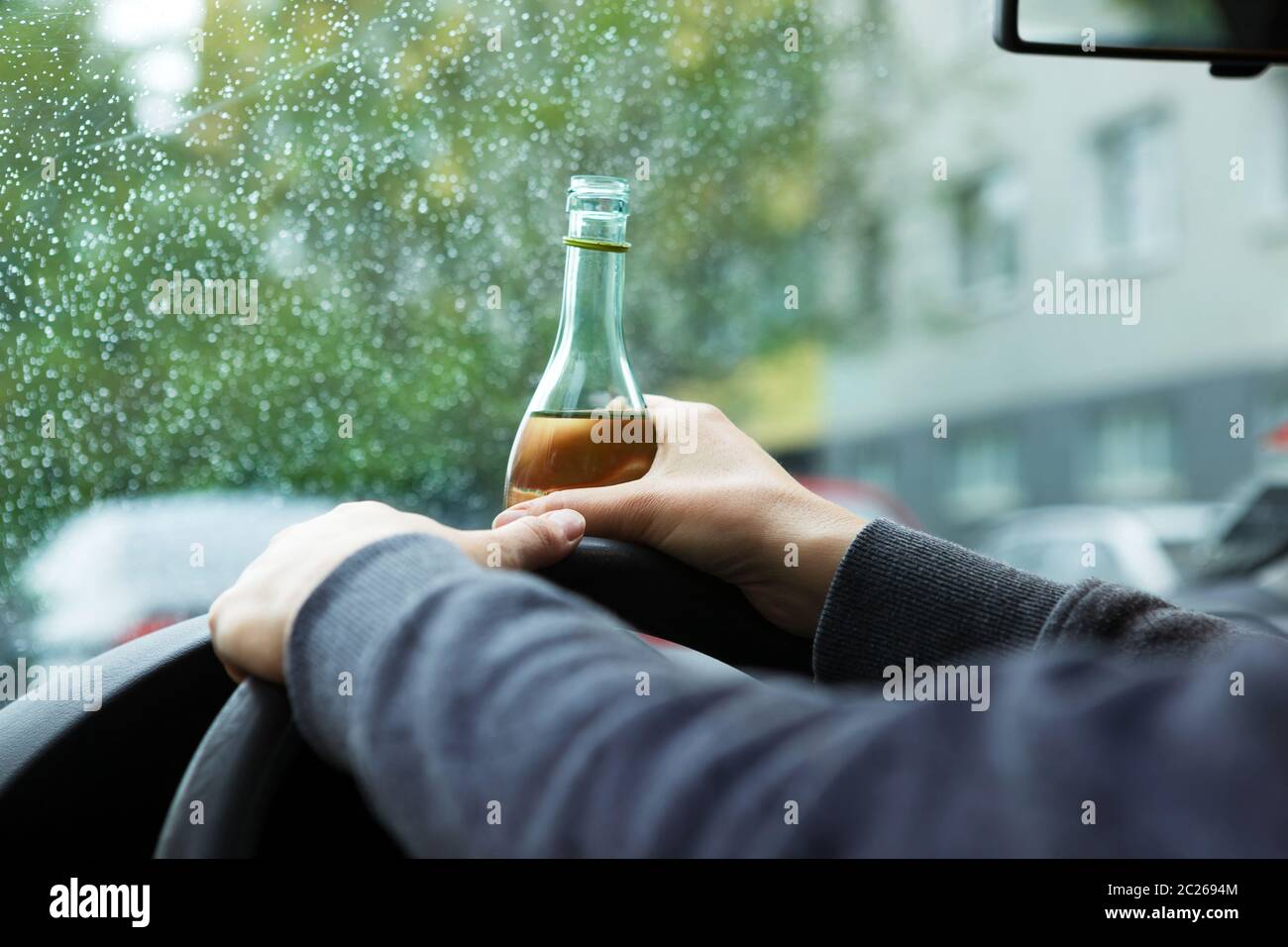 Betrunkener junger Fahrer, der während der Fahrt eine Flasche Wein trinkt. Stockfoto