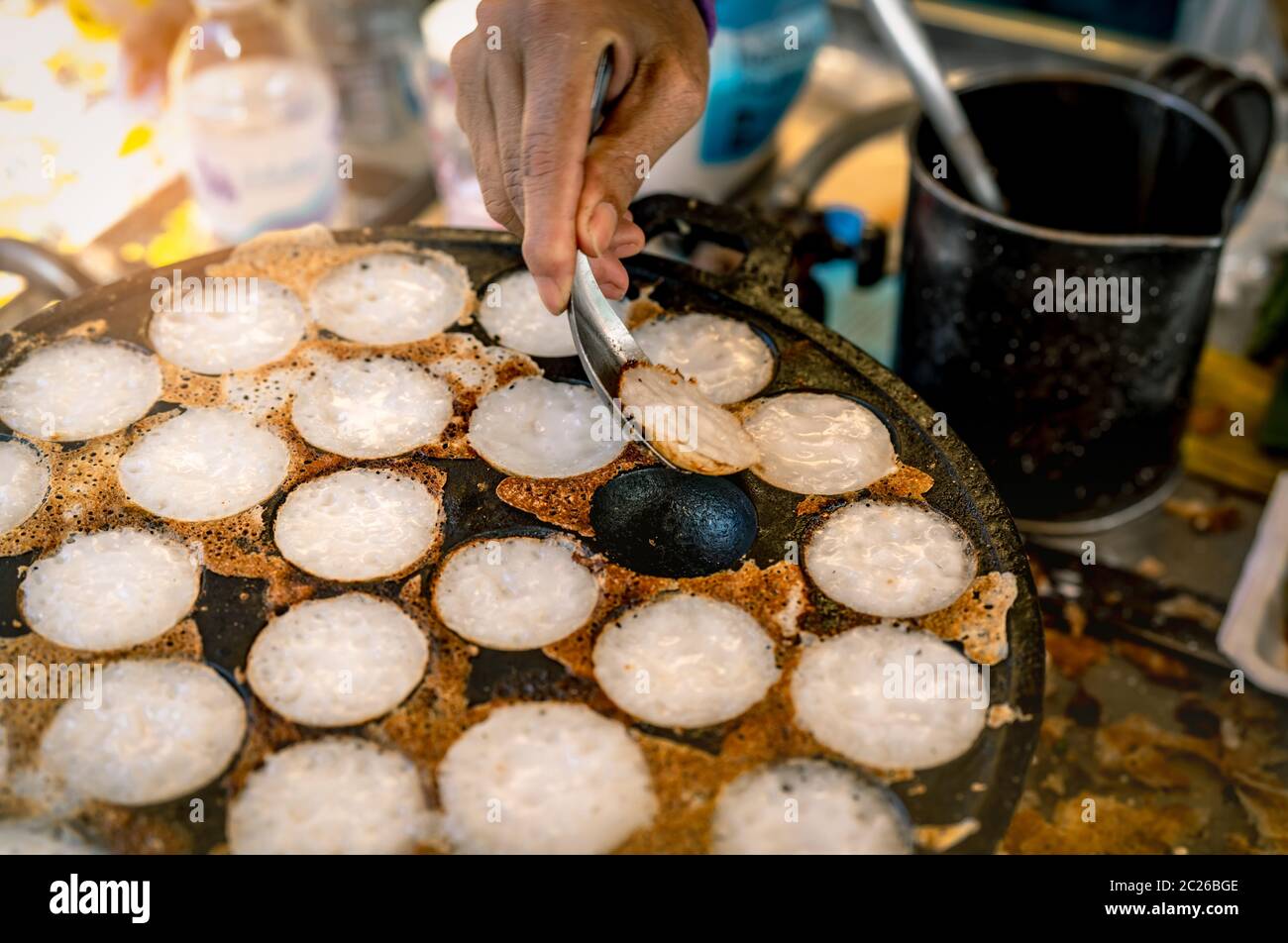 Mörtel - geröstete Gebäck oder "Kanom Krok' ist für traditionelle thailändische Dessert. Frau Hand entfernen Kanom Krok von Herd durch die Löffel. Street Food in Thailand. Thai d Stockfoto