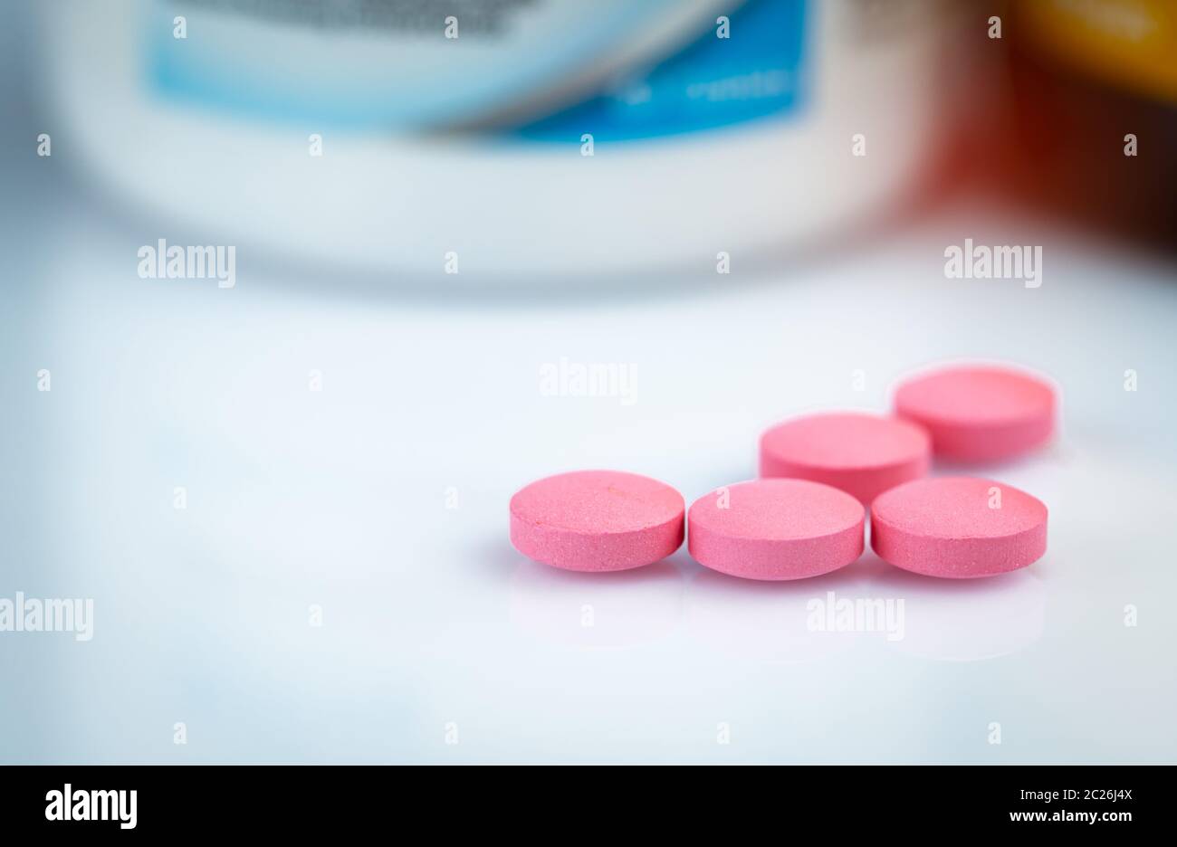 Runde rosa Tabletten Pille auf unscharfen Droge Flasche. Vitamine und Mineralien plus Folsäure, Vitamin E und Zink in der Droge Flasche auf farbverlauf Hintergrund. Rosa t Stockfoto