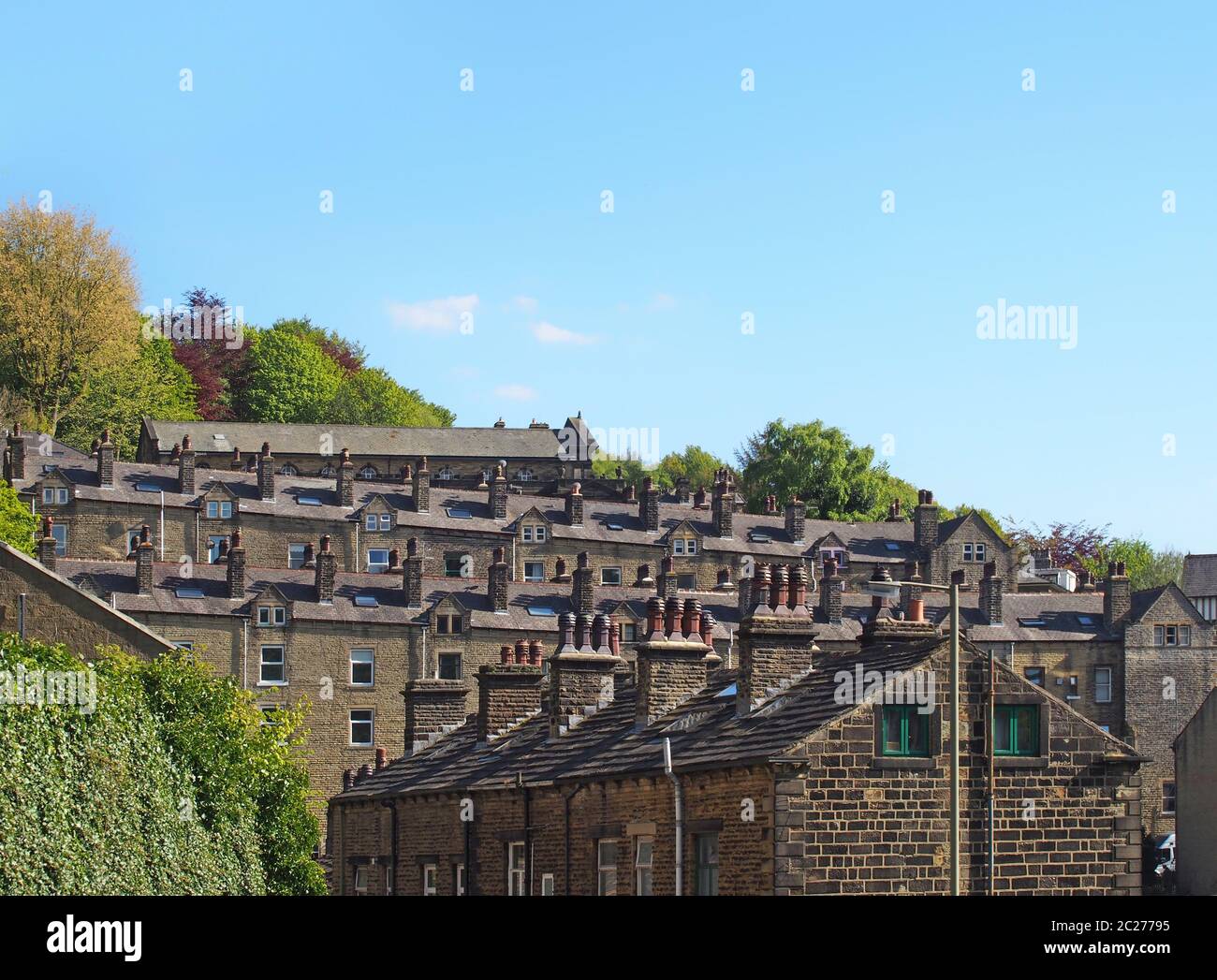 Straßen von terrassenförmigen Steinhäusern auf einem Hügel umgeben von Bäumen mit einem blauen Sommerhimmel in hebden Brücke West yorkshire Stockfoto