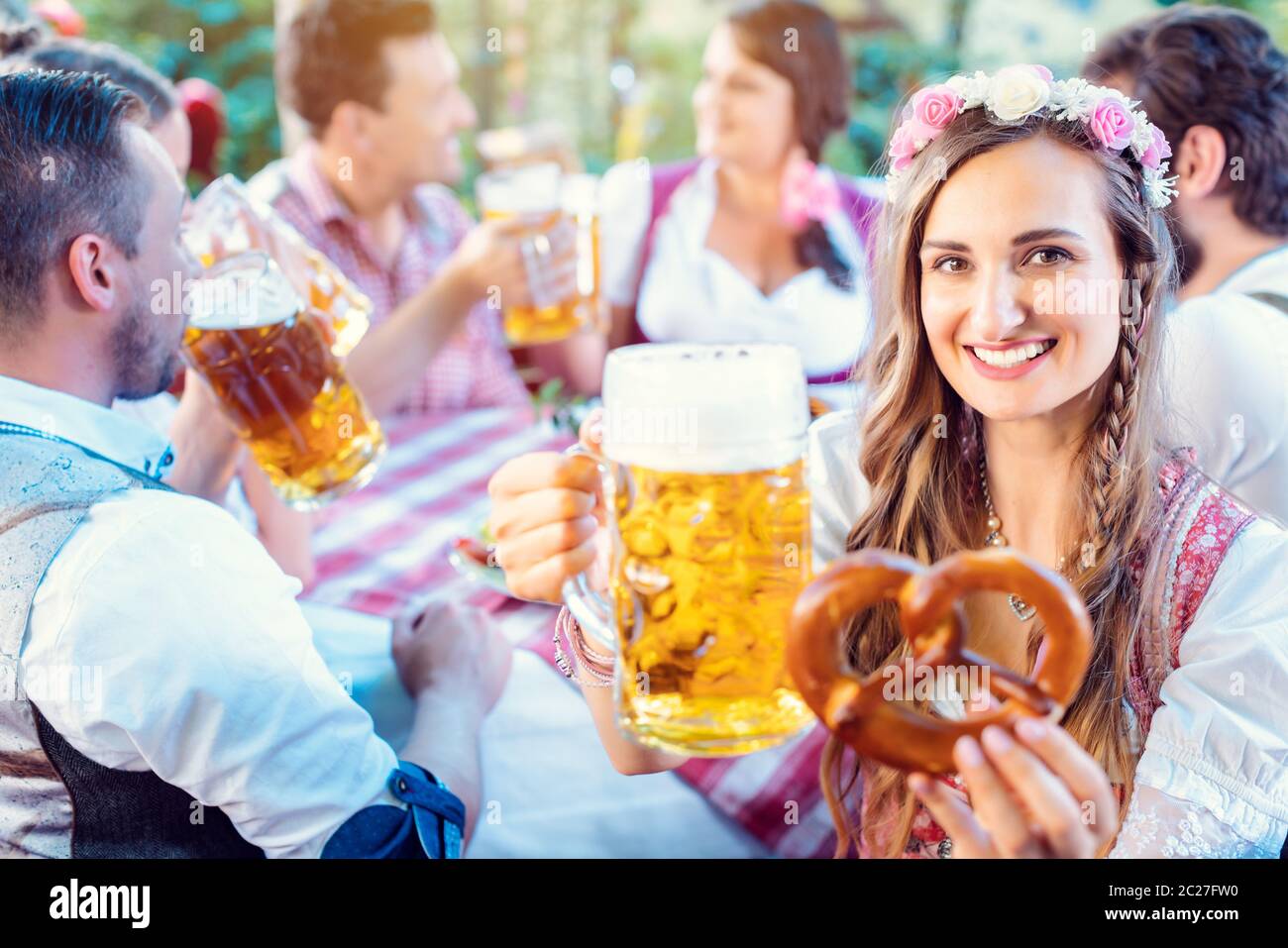 Frau, die mit einem Glas Bier in der bayerischen Kneipe mit Brezel in der Hand vor die Kamera schrunkt Stockfoto