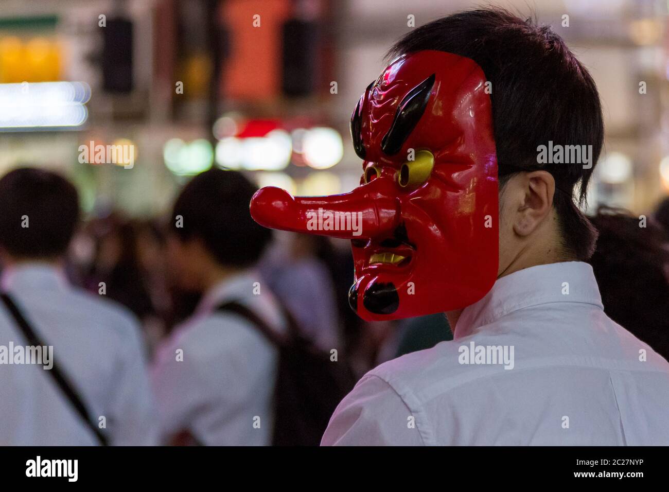 Ein junger Japaner trägt eine Tengu-Maske, als er Menschen für ein youtube-Video auf dem Hachiko Square, Shibuya, Tokio, Japan interviewt. Stockfoto