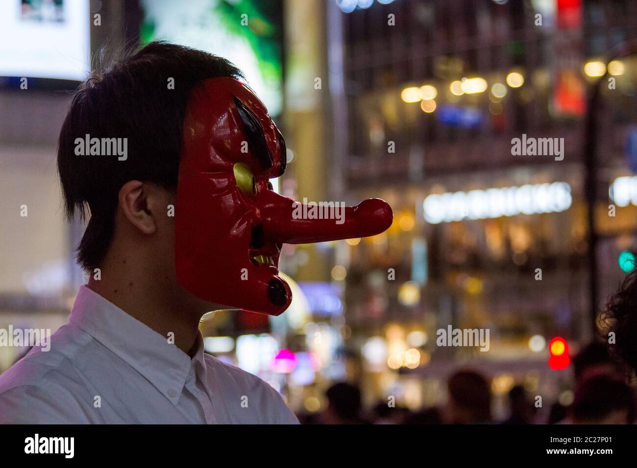Ein junger Japaner trägt eine Tengu-Maske, als er Menschen für ein youtube-Video auf dem Hachiko Square, Shibuya, Tokio, Japan interviewt. Stockfoto
