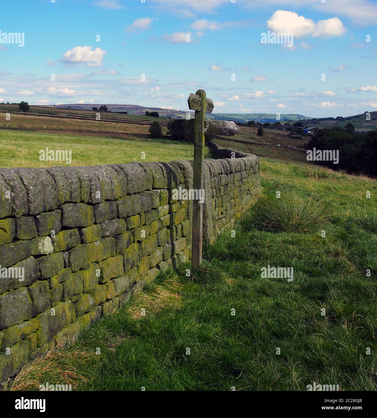 Die offene Landschaft mit Richtung neben einer Trockenmauer mit grünen Feldern und mooland in der Ferne in Yorkshire, England Stockfoto