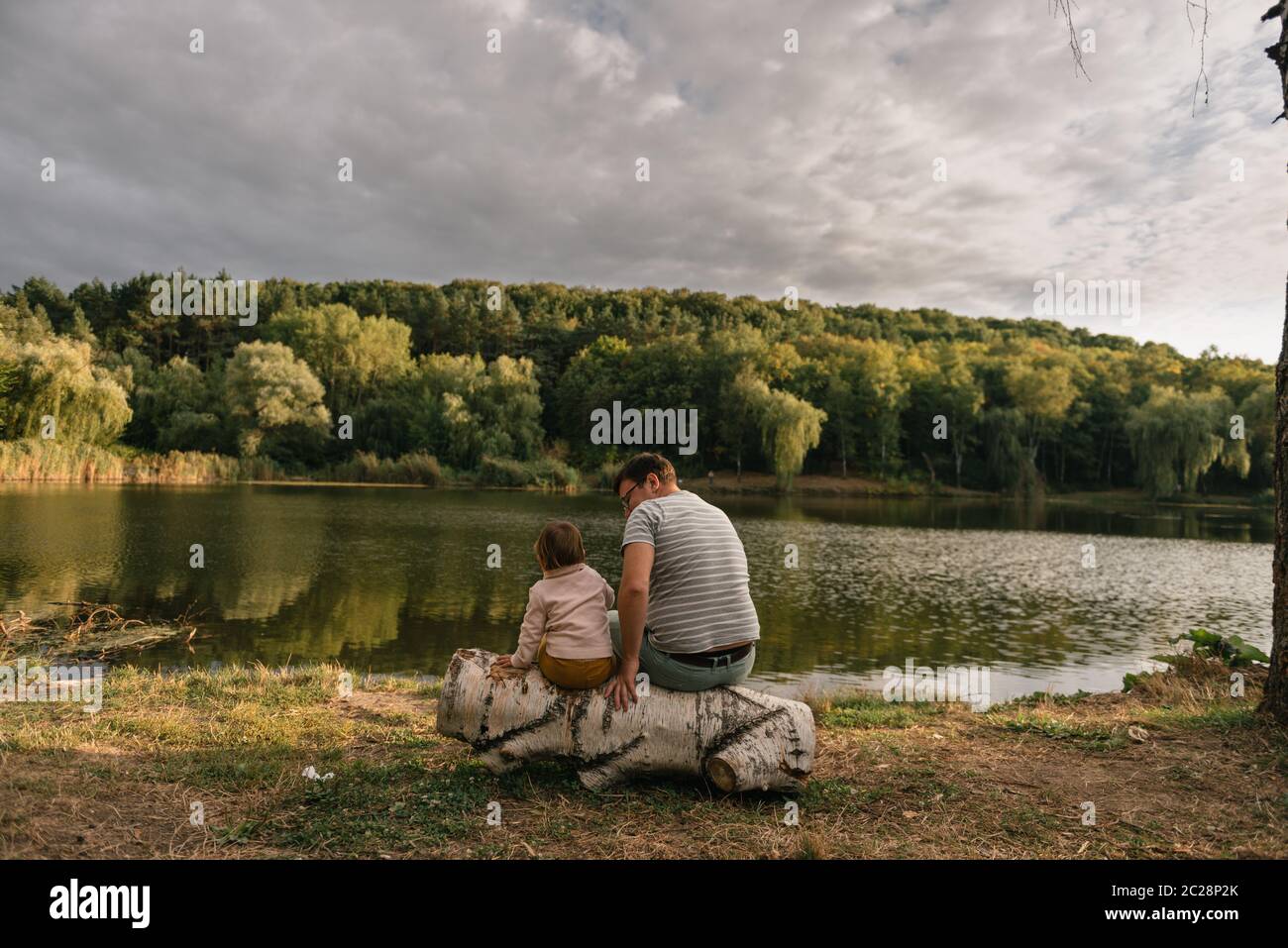 Vater und Baby Mädchen sitzen in der Nähe des Sees. Lokale Reisen. Neuer normaler Urlaub. Vatertag Stockfoto