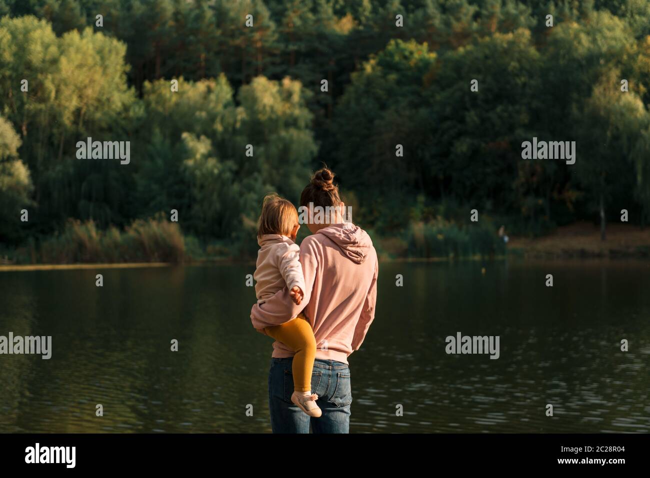 Mutter und Baby Mädchen sitzen in der Nähe von See. Lokale Reisen. Neuer normaler Urlaub. Muttertag Stockfoto