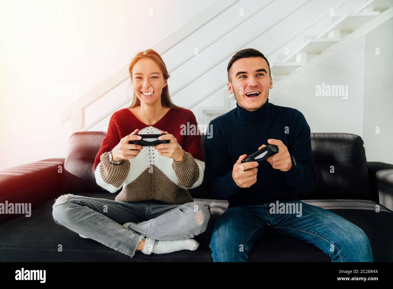 Glückliches junges Paar, sehr aufgeregt beim Spielen von Computerspielen mit Joysticks, sitzen auf der Couch, zu Hause. Stockfoto